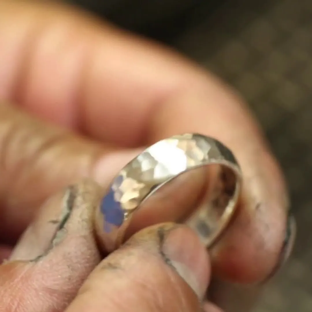 Anillo de banda ancha martillada y pulida, sostenido entre los dedos