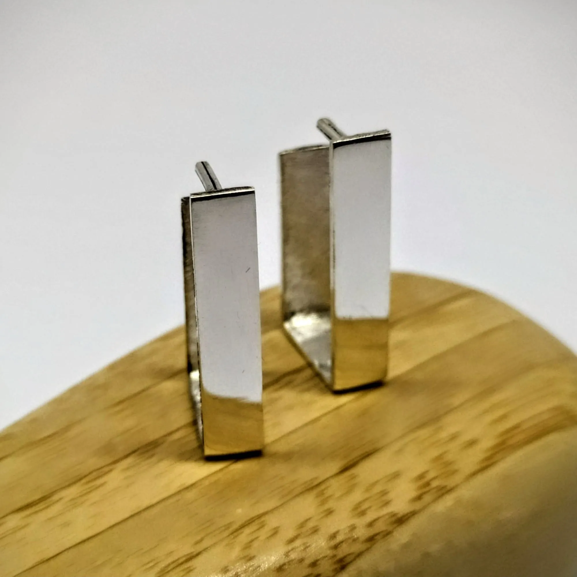 Par de aros rectangulares de plata pulida, parados sobre una base de madera